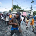 FILE - A protester carries a piece of wood simulating a weapon during a protest demanding the resignation of Prime Minister Ariel Henry, in the Petion-Ville area of Port-au-Prince, Haiti, Oct. 3, 2022.