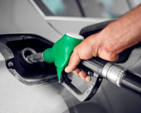 A man holds green fuel nozzle into the petrol tank of a car at the petrol station