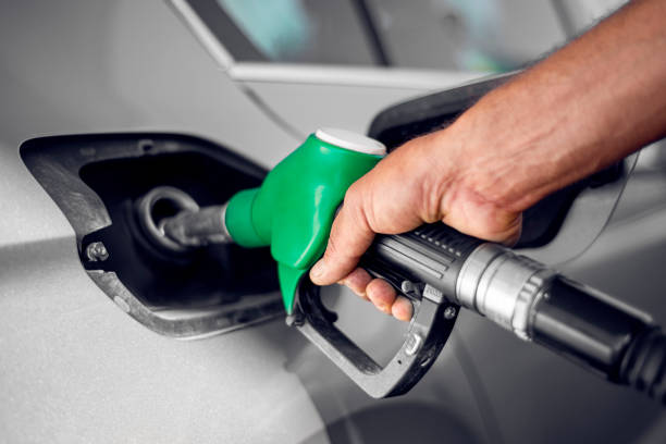 A man holds green fuel nozzle into the petrol tank of a car at the petrol station